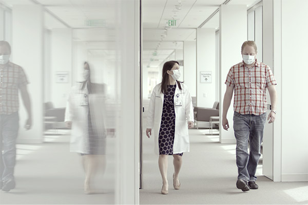 Female cancer provider walking and talking to male patient while wearing masks