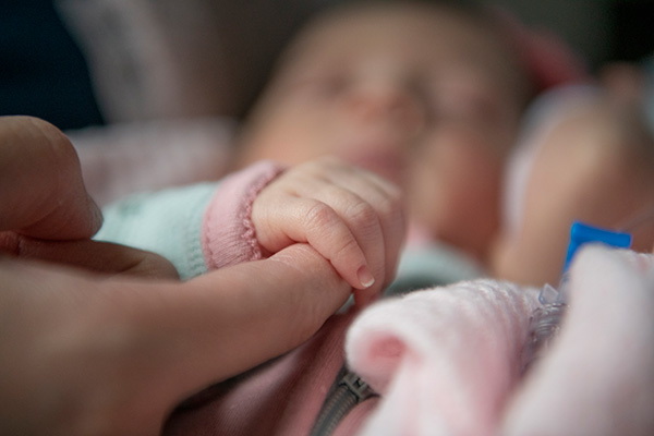 A close-up of a newborn holding a parent's finger