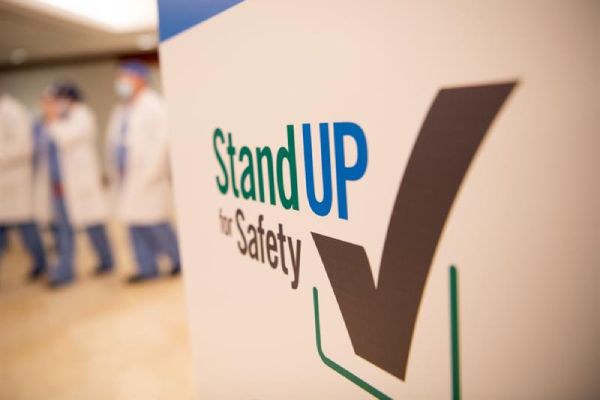 StandUP for Safety poster with doctors walking behind it.