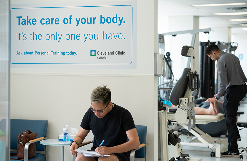 A person sitting in a chair filling out paperwork with a personal trainer working behind them