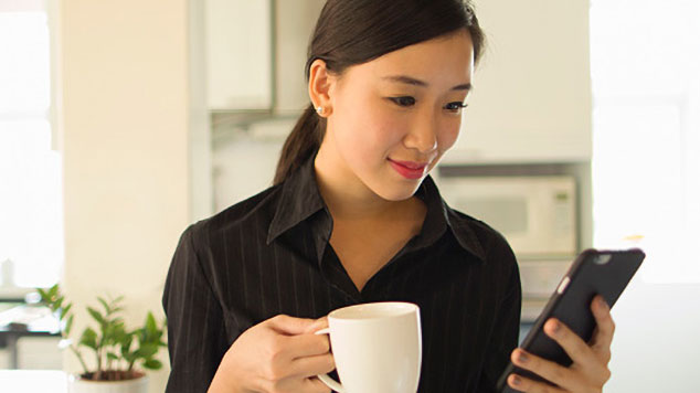 Woman holding a coffee mug in one hand, and her cell phone in the other.