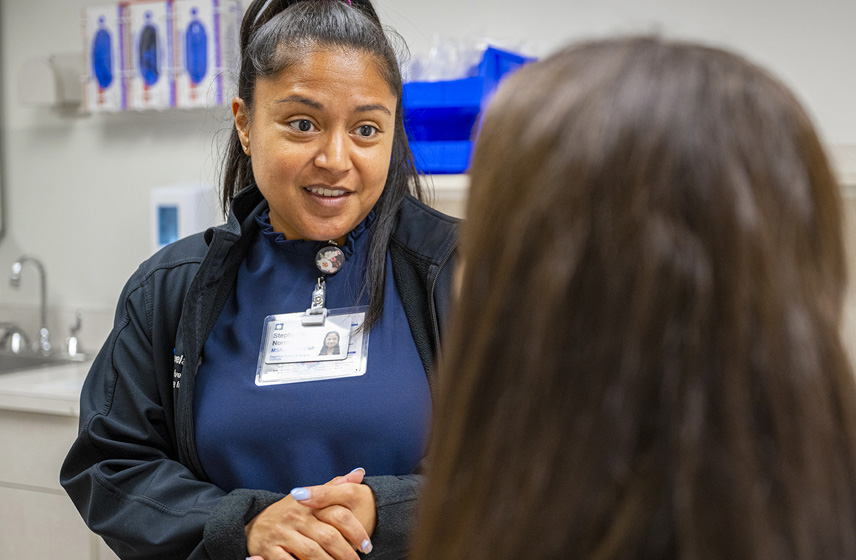 A Cleveland Clinic caregiver talking to a seated patient. Only the back of the patient's head is visible.