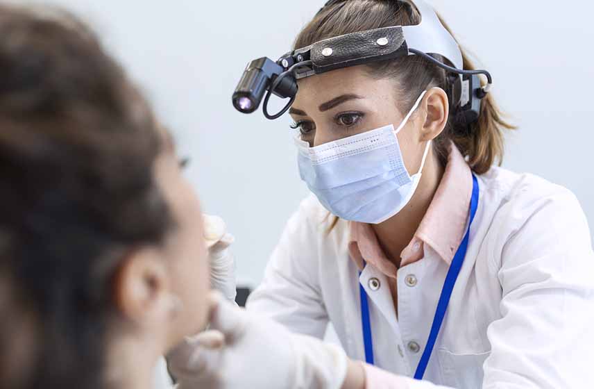 Cleveland Clinic doctor checking inside a patients mouth wearing gloves, a mask and a head lamp.