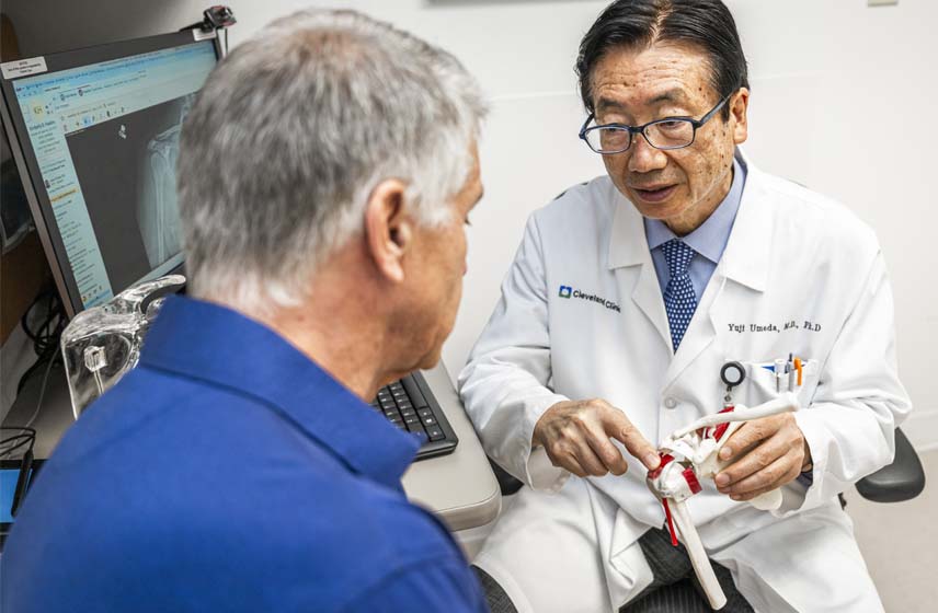 Cleveland Clinic doctor holding a model of a shoulder joint, speaking with a patient.