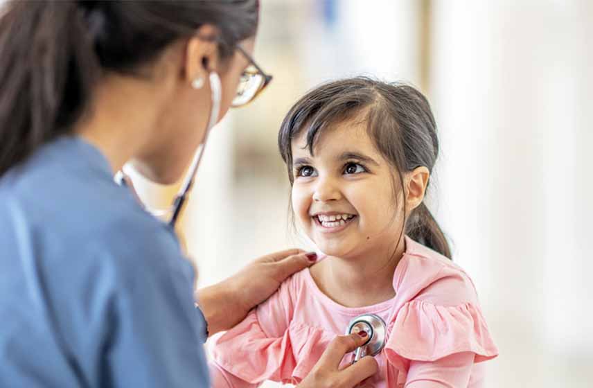 Young girl smiling as doctor examines her chest sounds with stethoscope.