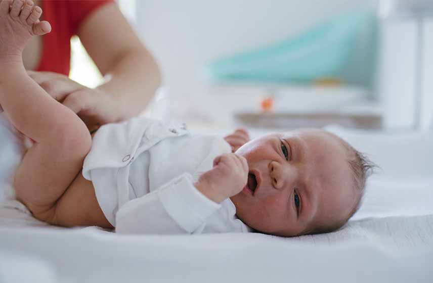 Newborn baby, with hands balled into fists, stretching on a diaper changing table.