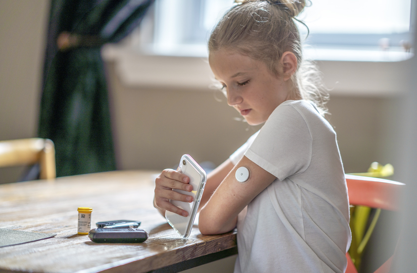 A child putting a smartphone up to a glucose monitor on her arm