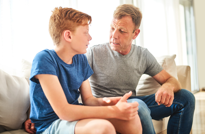 Teen boy talking to his father while sitting on the couch.