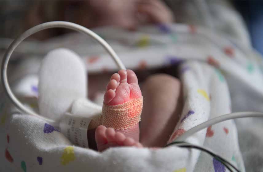 Newborn's foot connected to monitors and wires while swaddled in a blanket.