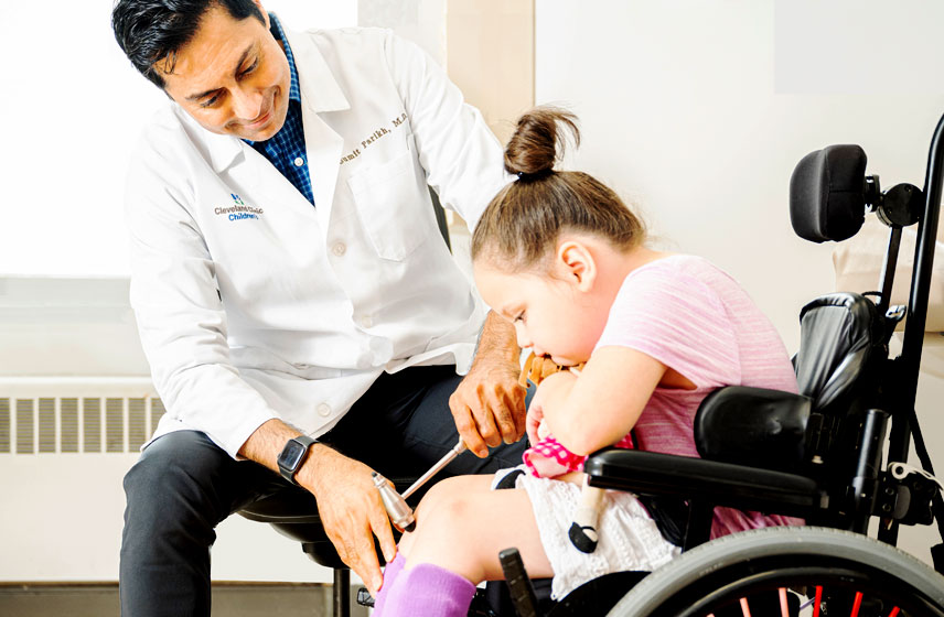 Doctor examining knee reflexes on a young girl sitting in a wheelchair.