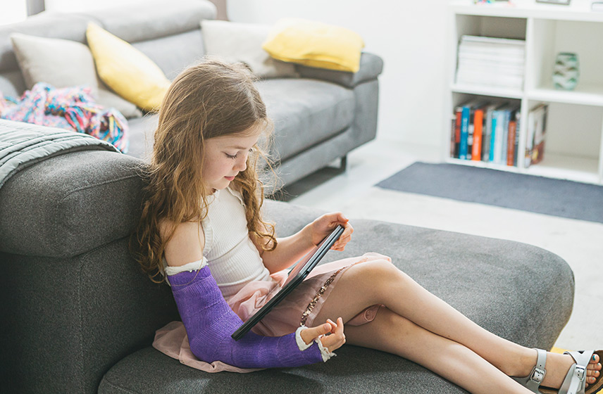 Young girl playing on a tablet with her broken arm in a purple cast.