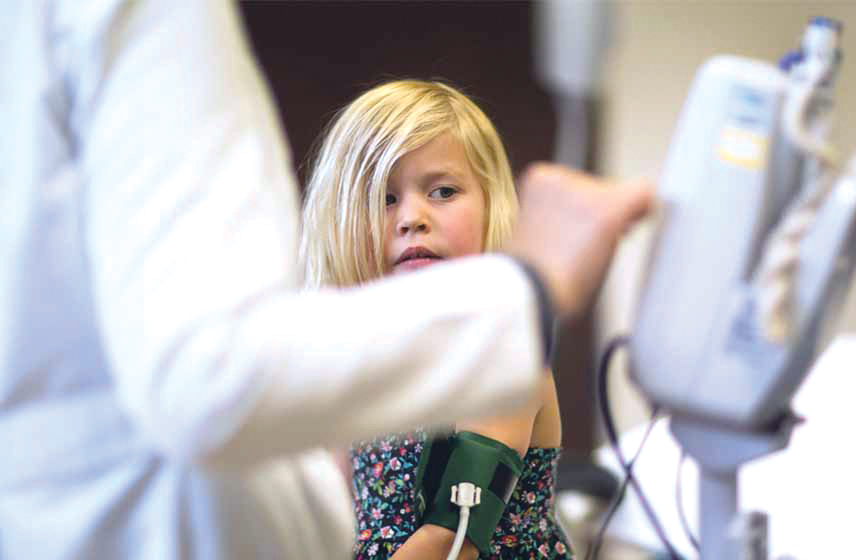 Doctor performing a blood pressure test on a young girl's arm.