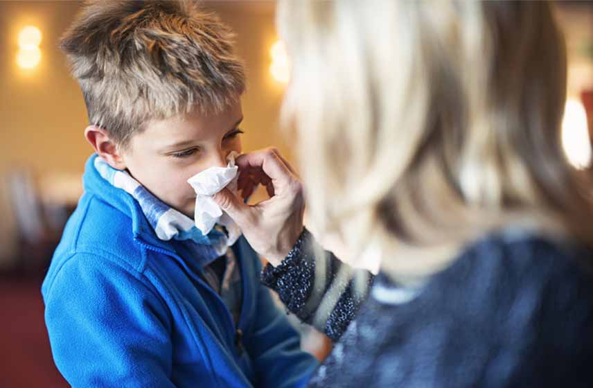 Woman holding a tissue to a boys' nose to stop it from bleeding.