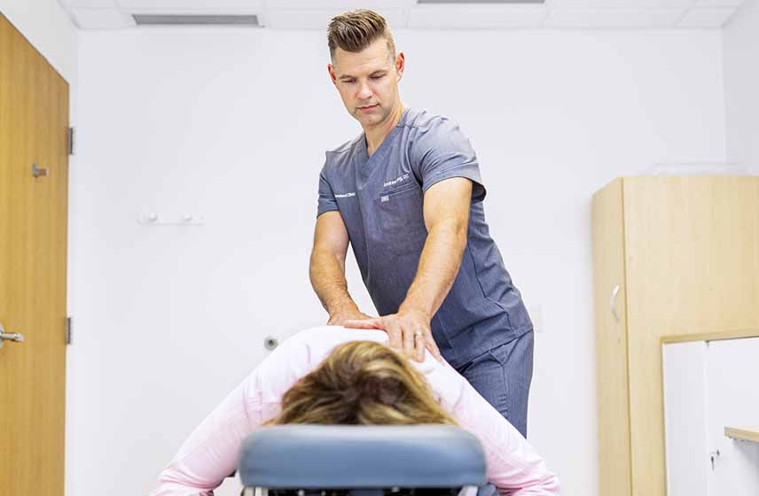Chiropractor massaging a patient's back while lying face down on a cushioned table.