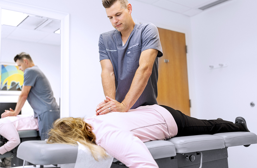 Chiropractor massaging a patient's back while lying face down on a cushioned table.