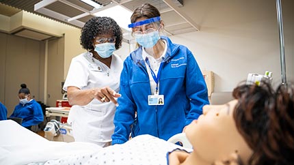 Nurse instructing student on simulator.