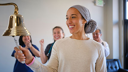 Visibly wearing a scarf to cover her head, a woman rings the bell following chemo treatment.