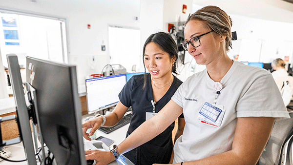Two nurses in scrubs examining patient files on a computer.