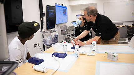 A Cleveland Clinic Caregiver looking at a computer screen along with several students.