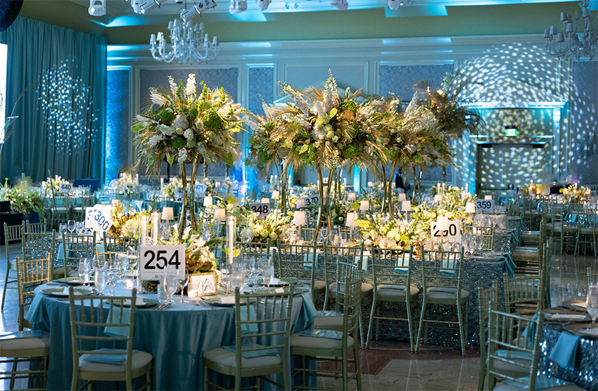 Image of a decorated ballroom with tables, chairs, and palm trees