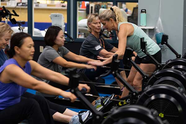 Female instructor assisting guest on rowing machine.