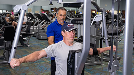Personal trainer helping man with upper-body exercise equipment.