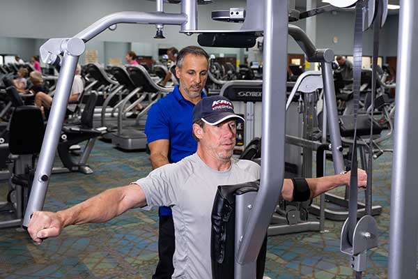 Personal trainer helping man with upper-body exercise equipment.