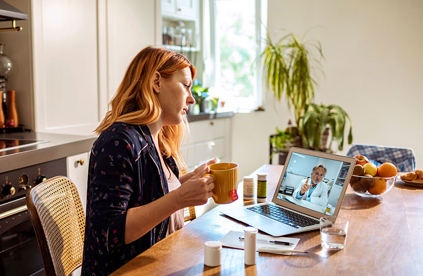 Female patient sitting at the table on a video call, speaking with her doctor.