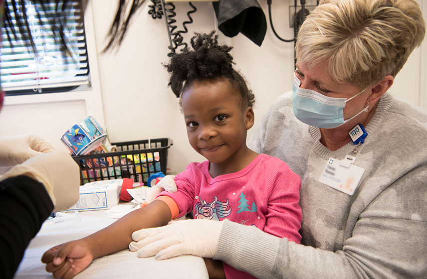 Cleveland Clinic Nurse sits with young girl as she receives her shot.