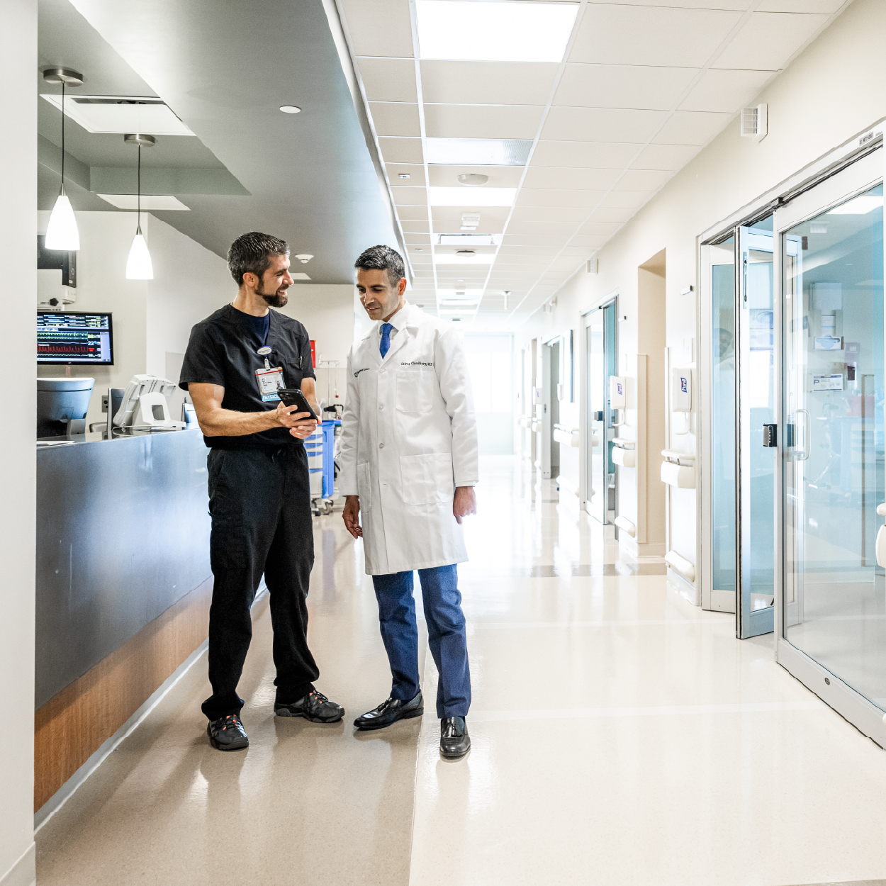 A professional caregiver stands at the bedside of a patient with a mobile device facilitating a virtual checkup