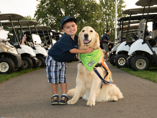 Five-year old Brooks Campbell, the unofficial ambassador of the Cleveland Clinic Children's golf outing, hugs Kid, one of Cleveland Clinic Children's specially trained facility dogs, on August 28, 2023.