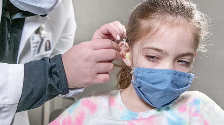Audiologist placing hearing aid in pediatric patient's ear