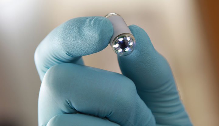 Gloved hand holding pill-sized camera used in capsule endoscopy.