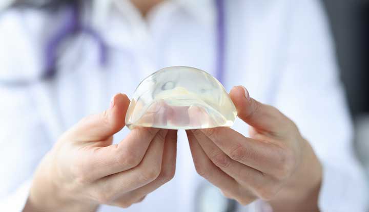 A provider holding a breast implant that looks like a clear silicone shell filled with gel.