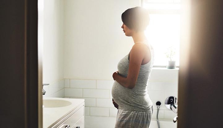 Pregnant woman standing in bathroom while holding her belly