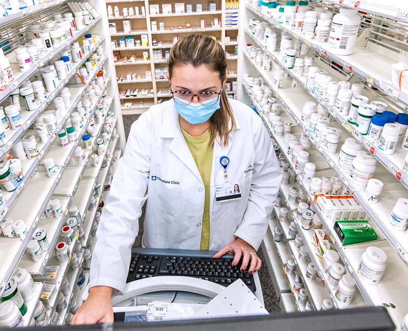 Surrounded by medicines in a pharmacy, a pharmacist fills a prescription.