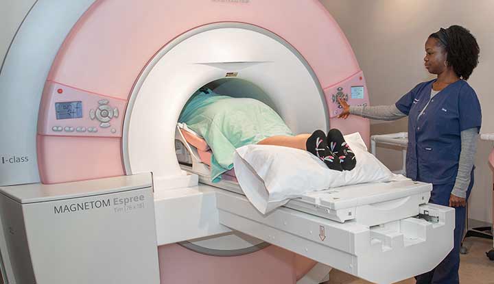 A person lying on their stomach on an exam table going head-first into the opening of an MRI machine, shaped like a donut.