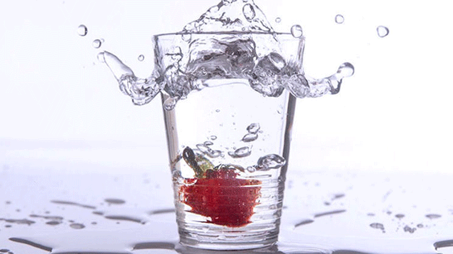 Glass of water with a strawberry in it.