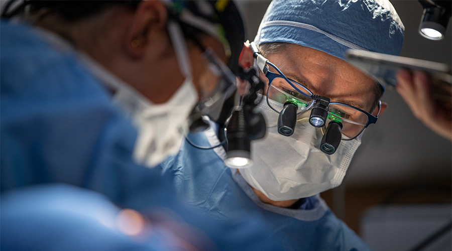 A doctor in scrubs and a face mask performing surgery.