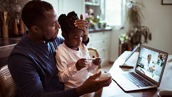 Man with daughter on his lap during video chat with their doctor