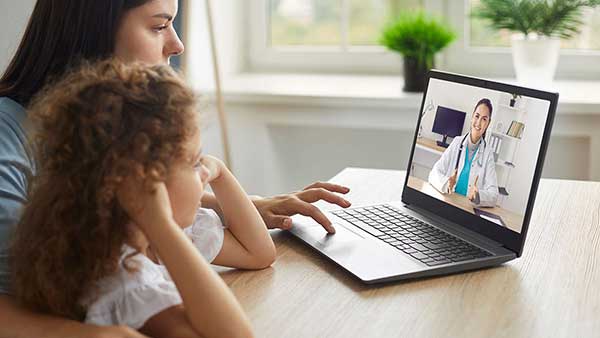 Parent with child having a virtual call with a physician on a laptop computer.