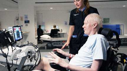 David Smith using a rehabilitation therapy bike while a Cleveland Clinic London physical therapist provides guidance.