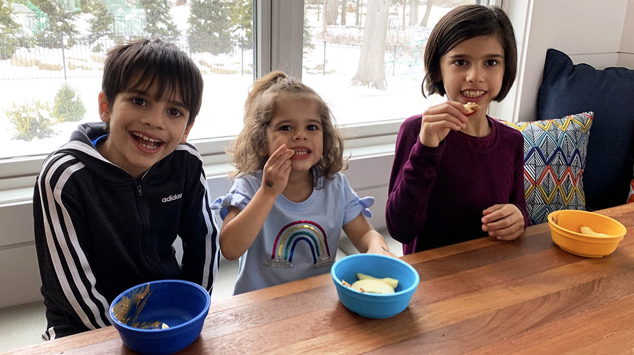 Harper eating apples with peanut butter alongside her brother and sister. 