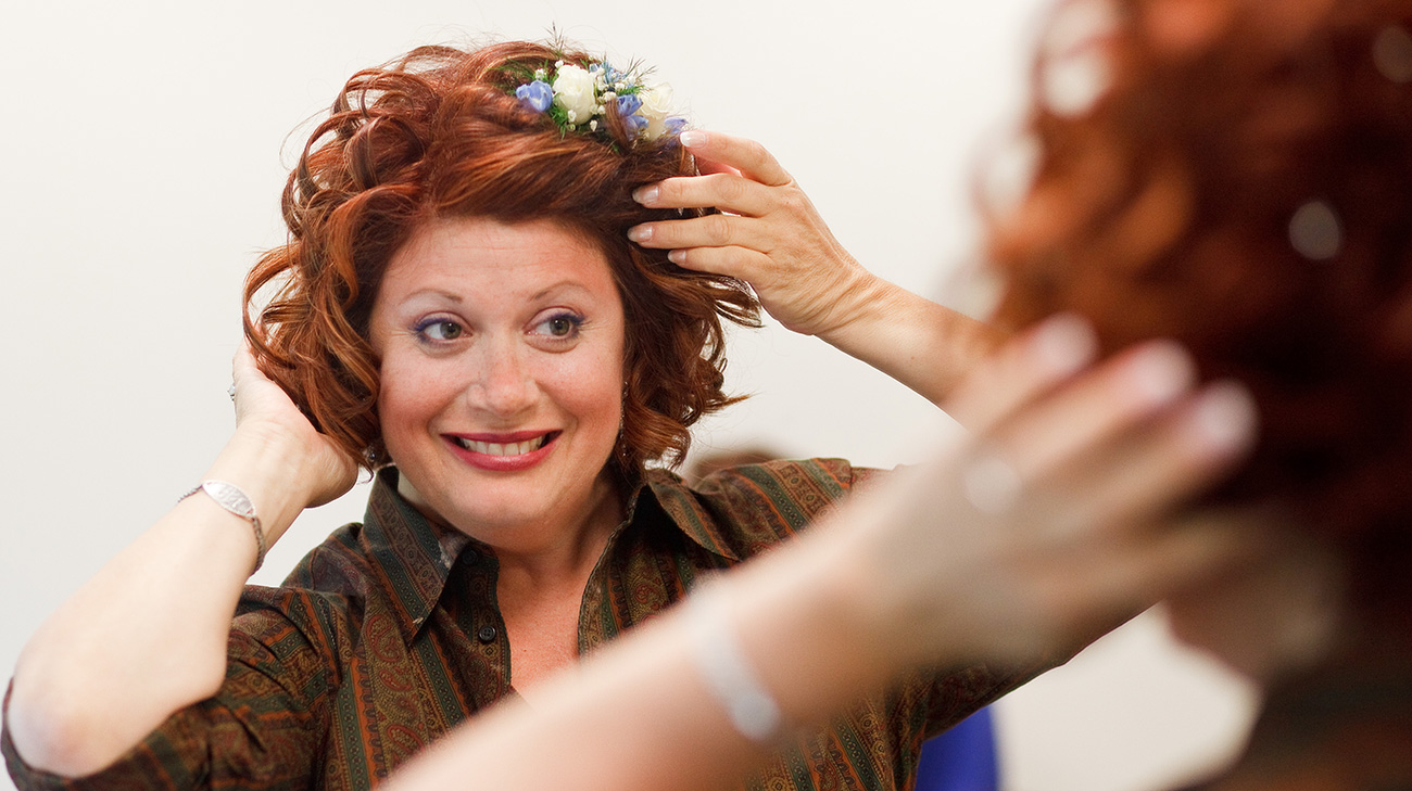 Sharon styling her hair in the mirror, with a big smile on her face.