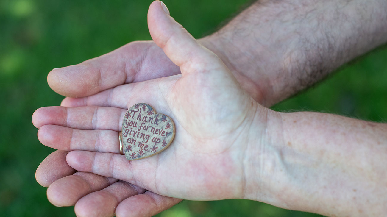 Don and Traci Hiltz holding a heart-shaped pendant that reads 'Thank you for never giving up on me.'