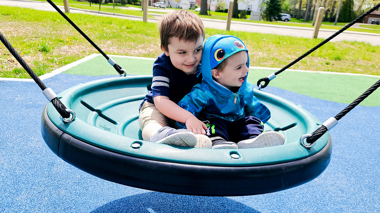 Johnny and Oliver on a swing in a playground.