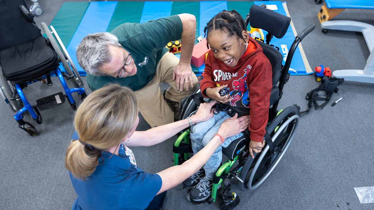JaLontae Price smiling and expressing excitement while Cleveland Clinic Children's outpatient therapists adjust his wheelchair.