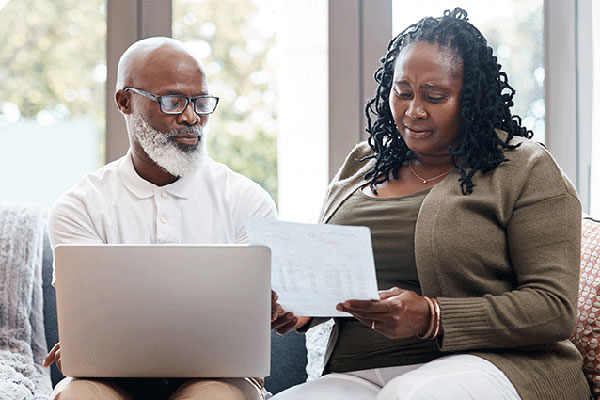 Older couple sitting on the couch, looking at a computer together.