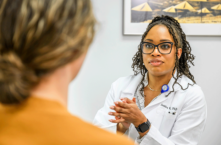 A person sitting in a medical exam room places a hand on their chest while speaking with a healthcare professional.