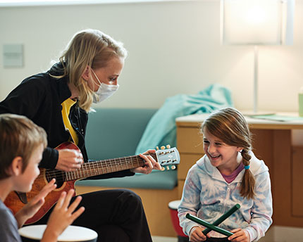 Music therapist playing guitar to children sitting in a circle playing other instruments.